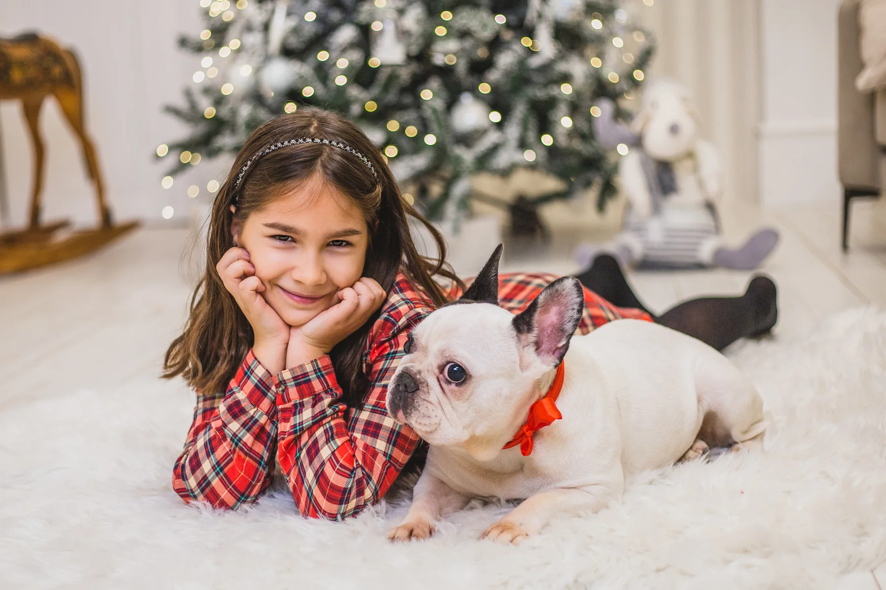Kislány mosolyog a francia bulldogja mellett egy puha szőnyegen