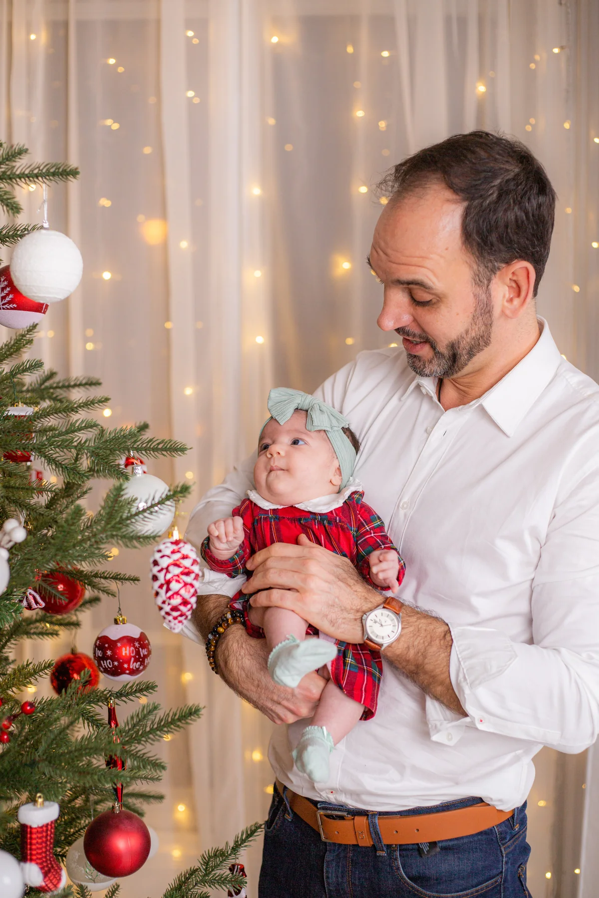 Apa gyengéden nézi kisbabáját a karácsonyfa mellett