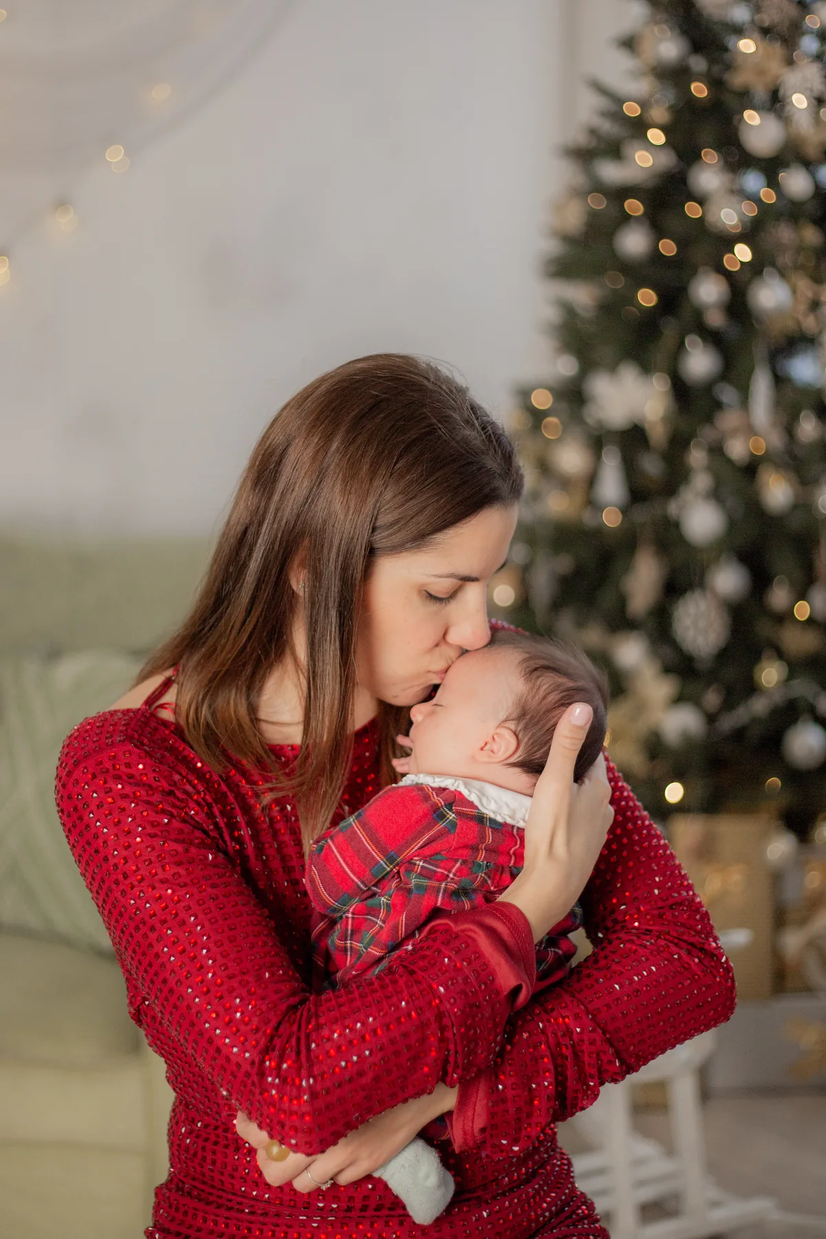 Anya puszit ad kisbabája homlokára a karácsonyfa mellett